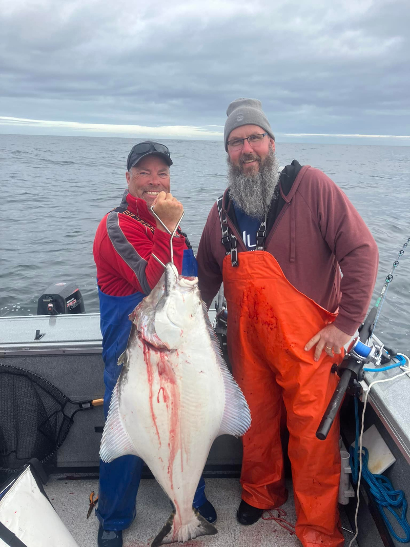 Two anglers holding a large Pacific halibut on a fishing boat off the coast of Newport, Oregon during a successful ocean halibut fishing trip