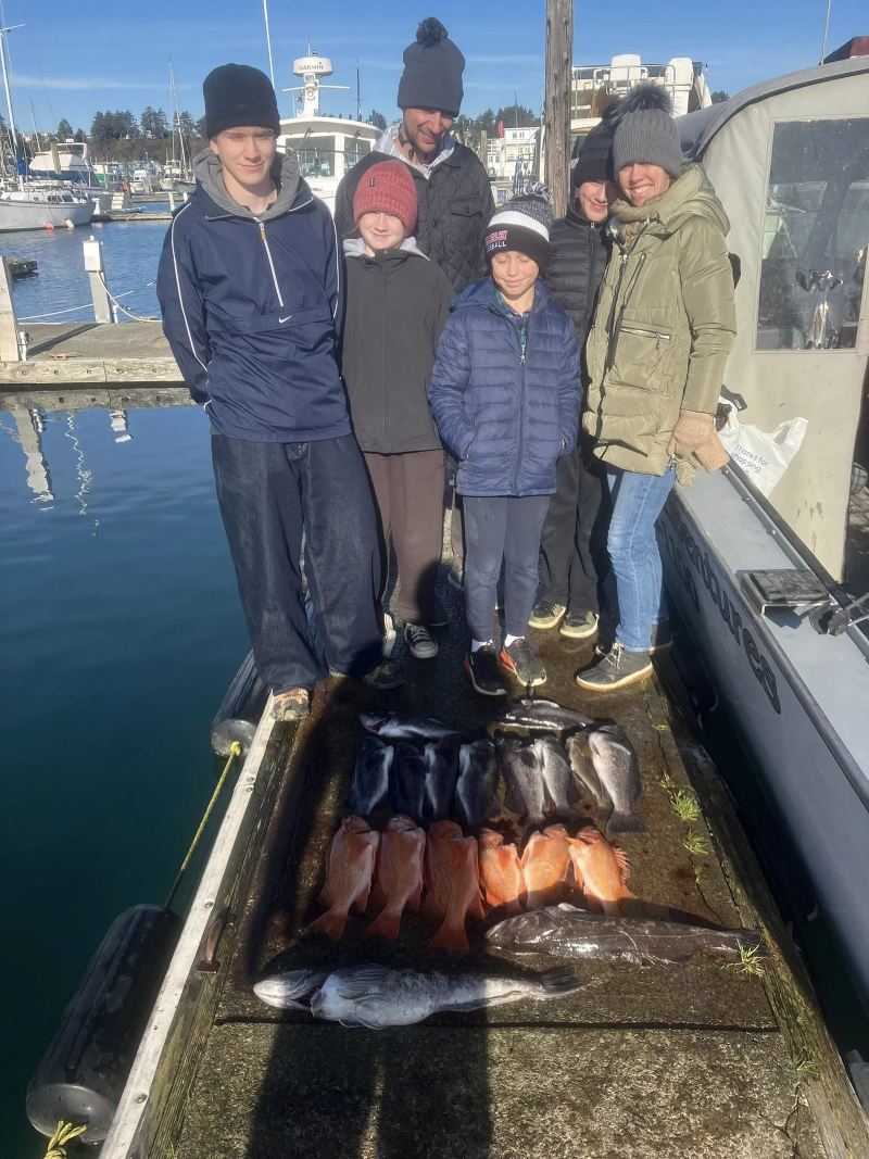 A family of six posing on a dock at Depoe Bay marina with their catch of bright orange Canary Rockfish and large Lingcod.